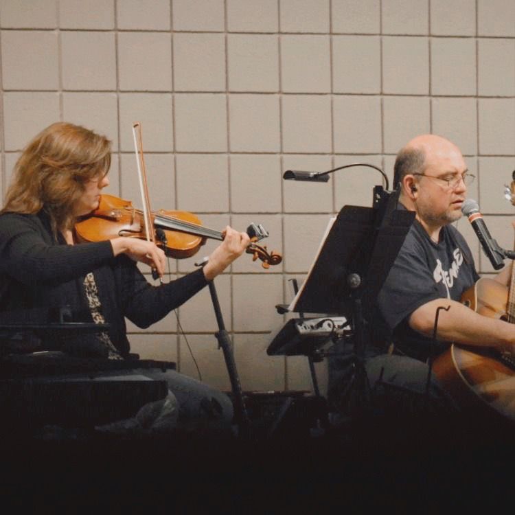 woman playing violin and man playing guitar in church